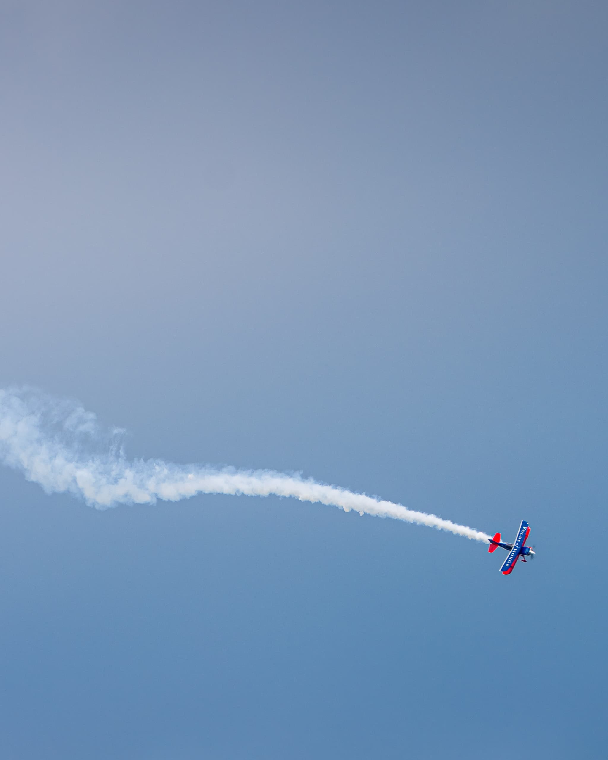 Stunt plane trailing white smoke across a hazy sky