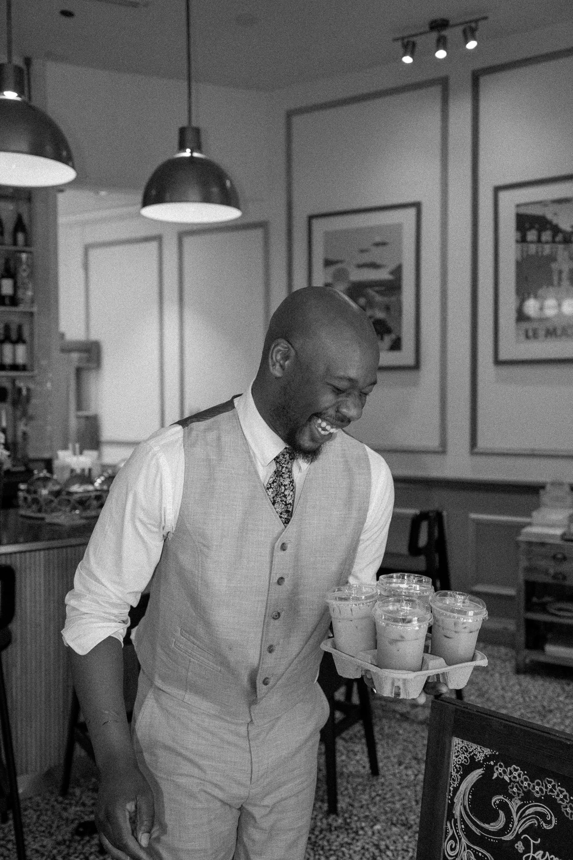 Black and white photo of a smiling server in a vest carrying a tray of drinks