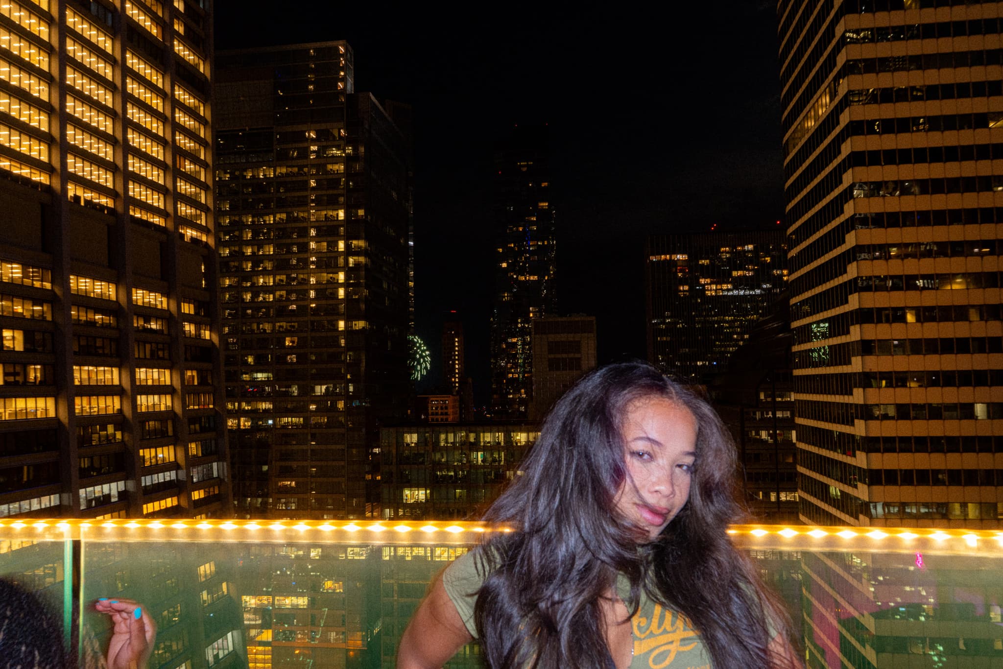 Woman with long hair smiling in front of lit downtown towers at night