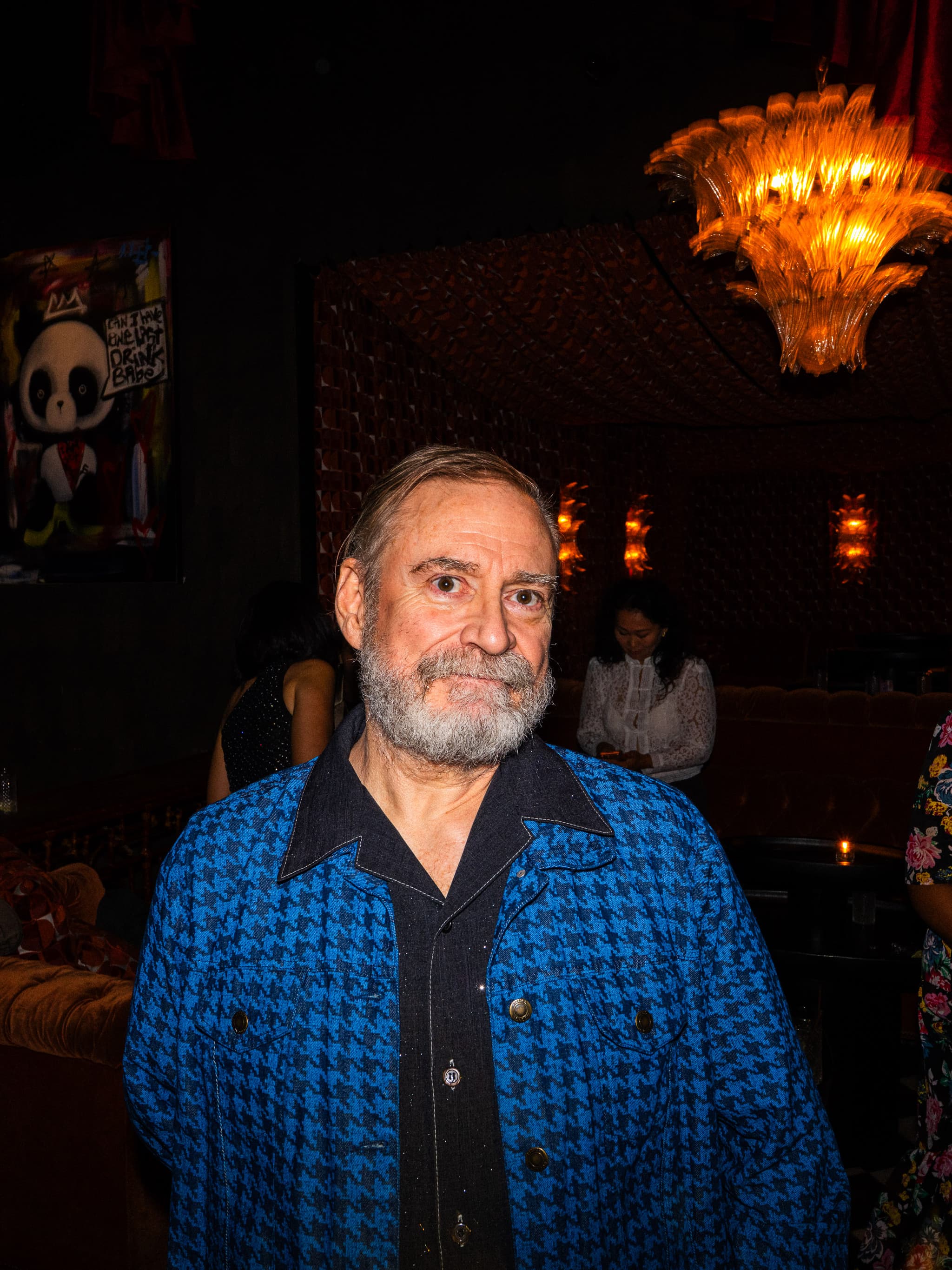 Man with a grey beard in a blue houndstooth jacket in a warmly lit room