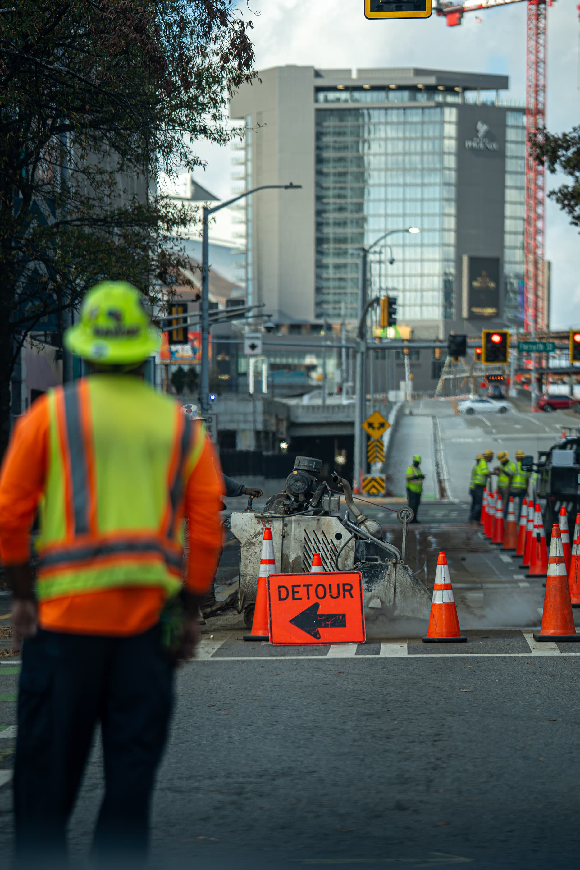 Construction worker in a hi-vis vest beside an orange detour sign downtown