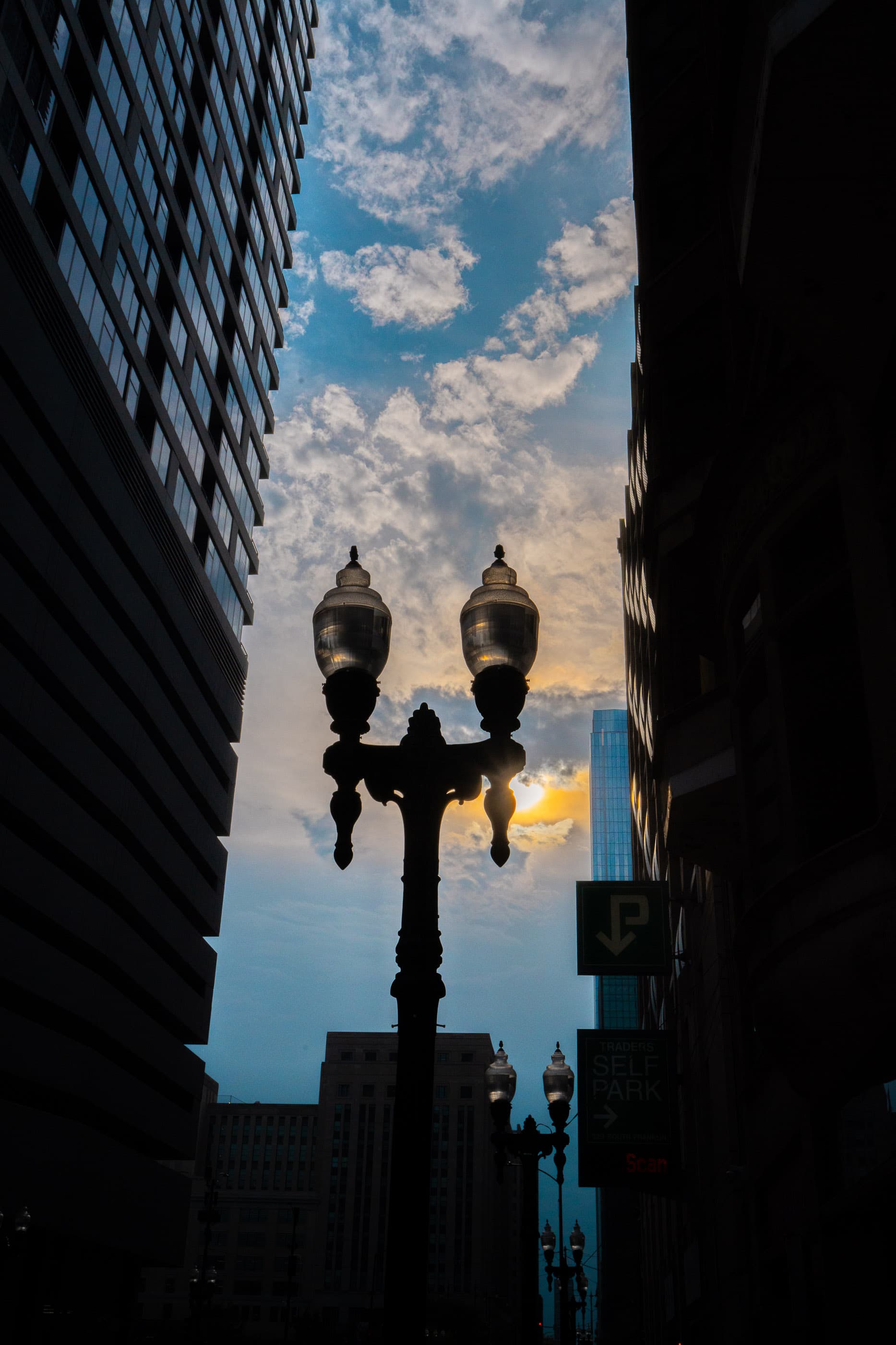 Ornate street lamp silhouetted between dark buildings at sunset