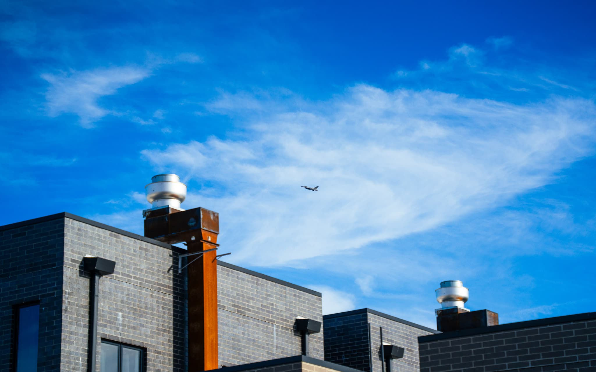 Plane passing over rooftop chimneys under a deep blue sky