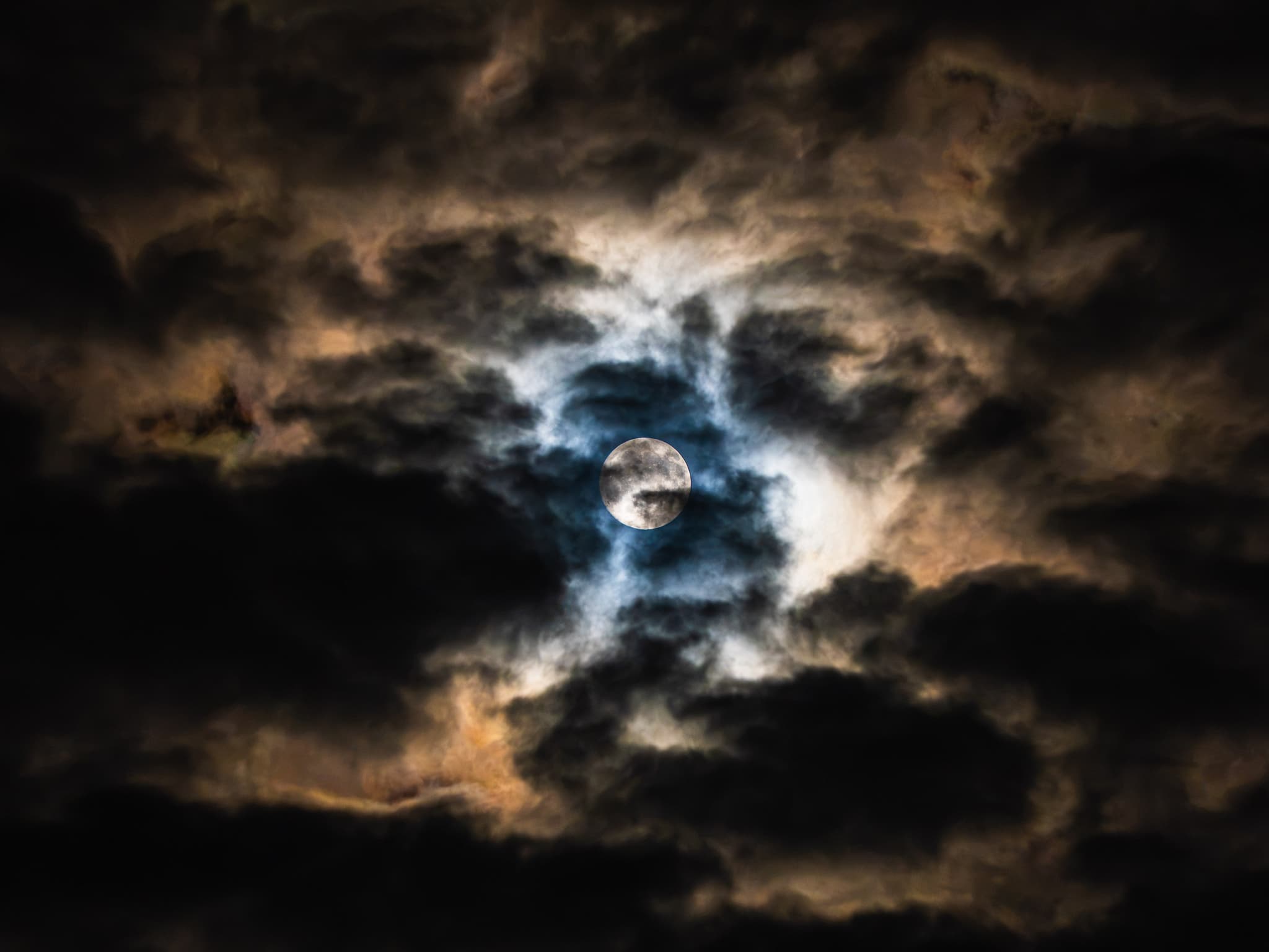 Full moon breaking through dark, backlit clouds at night