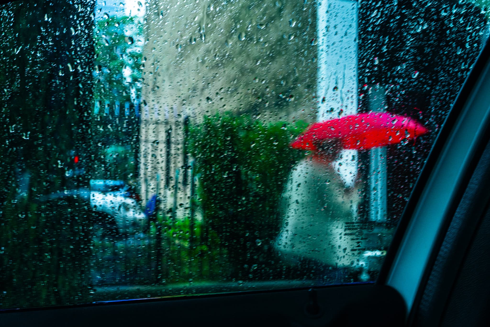 A red umbrella seen through a rain-covered car window