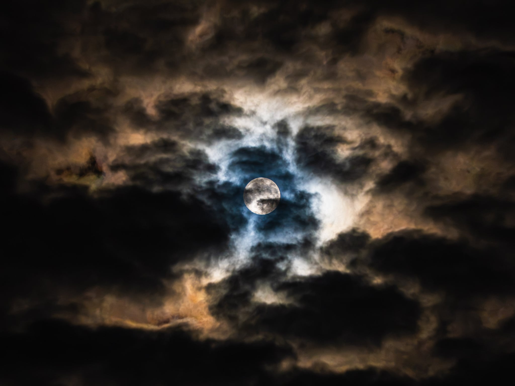 Full moon breaking through dark, backlit clouds at night