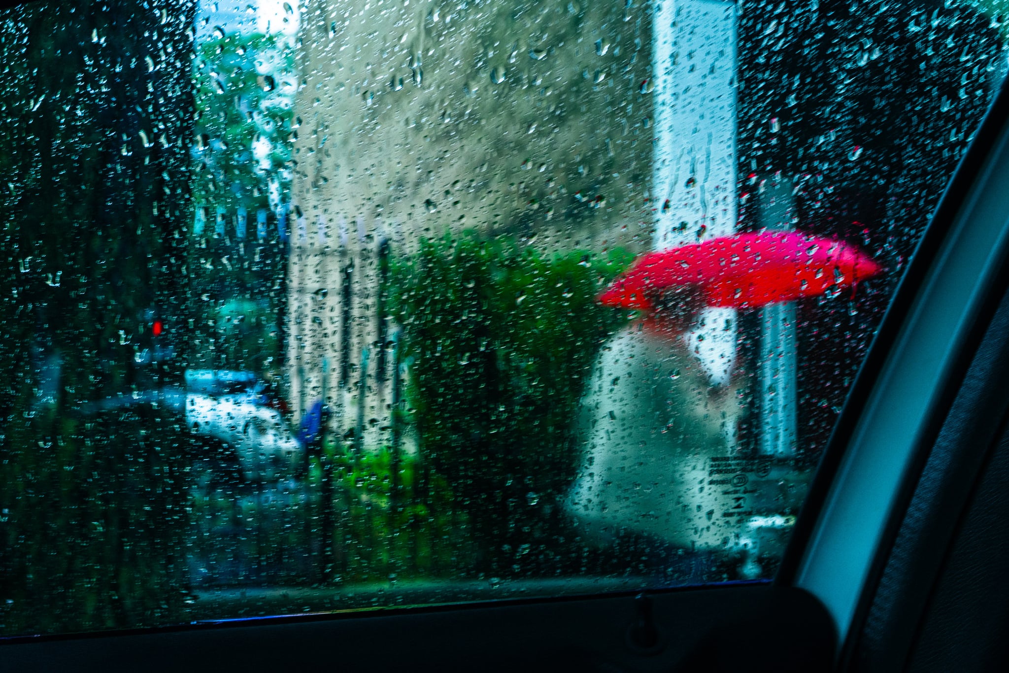 A red umbrella seen through a rain-covered car window